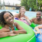 five people in colourful blow up tubes in a resort style pool gather and smile in a relaxed holiday picture.