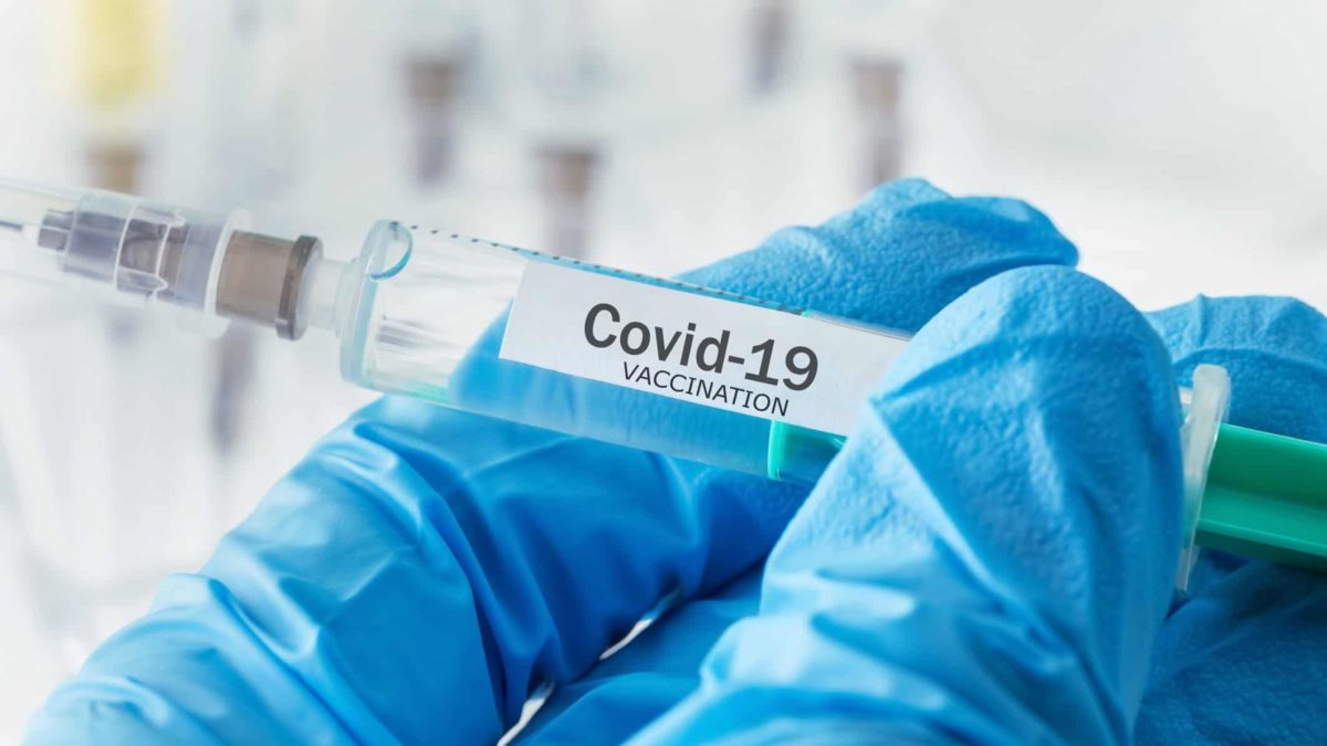 Gloved hands holding COVID-19 vaccine syringe