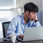 Falling ASX share price represented by young male investor sitting sadly in front of a laptop.