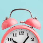 close up of pink alarm clock against blue background