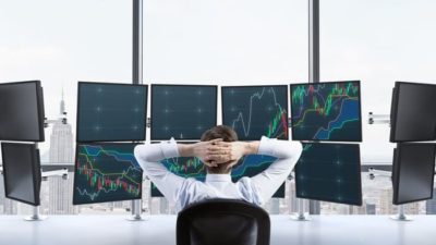 Investor sitting in front of multiple screens watching share prices