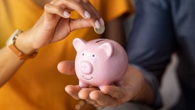 a happy pink piggy bank being held as a coin is dropped into the slot, indicating savings