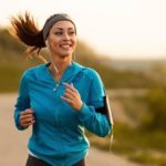 A female dressed in sports gear smiles as she runs along a road, indicating a positive share price for sports apparel companies