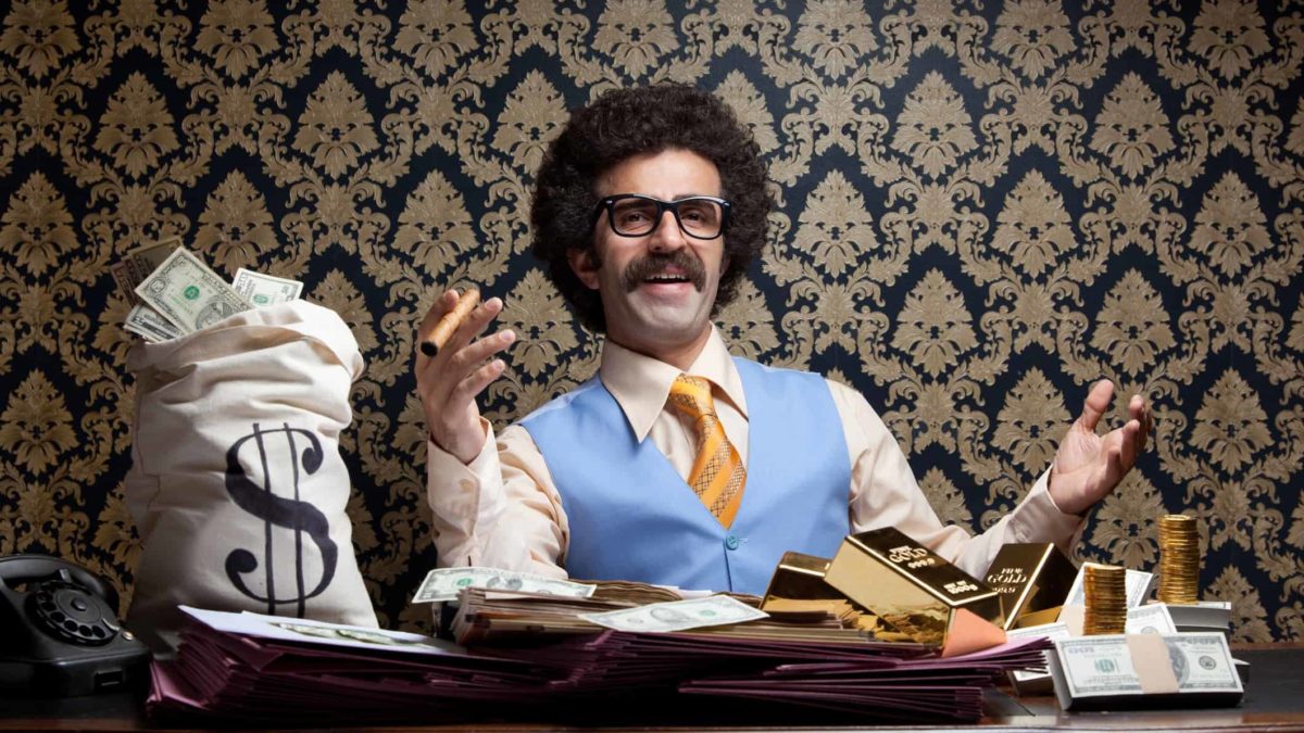 Rich man posing with money bags, gold ingots and dollar bills and sitting on table