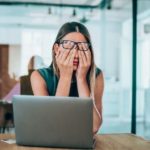 Investor covering eyes in front of laptop