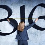 A woman holds a tape measure against a wall painted with the word BIG, indicating a surge in gowth shares