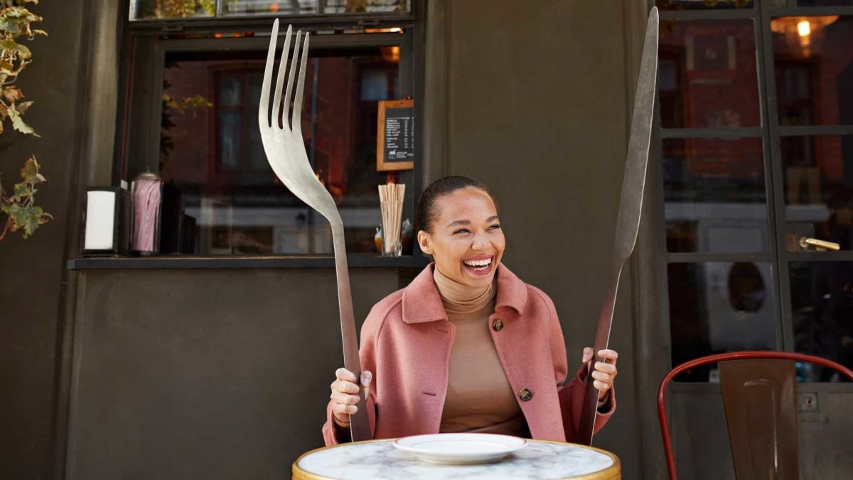 Woman dining at a table with oversized fork and knife in the hospitality industry.
