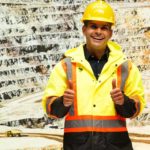 A smiling miner wearing a high vis vest and yellow hardhat and working for Superior Resources does the thumbs up in front of an open pit copper mine, indicating positive news for the company's share price today following a significant copper discovery