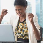 A happy woman at her laptop punches the air, indicating a rising share price