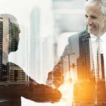 two businessmen shake hands amid a backdrop of tall buildings, indicating a share price movement or merger between ASX property companies