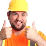 Mining worker wearing hard hat and high vis vest holds thumbs up and smiles