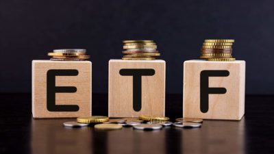 The letters ETF on wooden cubes with golden coins on top of the cubes and on the ground