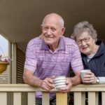 A elder man and woman lean over their balcony with a cuppa, indicating share rpice movement for ASX retirement shares