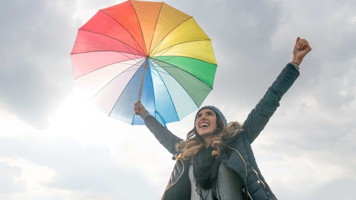 A happy looking woman holding a colourful umbrella against a grey cloudy sky.