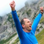 An excited man stretches his arms out above his head as he reaches a mountain peak representing two ASX 200 shares reaching multi-year high prices today