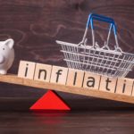 inflation written on wooden cubes being balanced with a piggy bank and small shopping basket