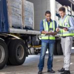 two men talking in front of a transportation truck