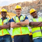 Three happy miners standing with arms crossed at a quarry.