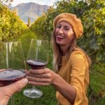 Happy smiling young woman drinking red wine while standing among the grapevines in a vineyard.