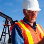 oil and gas worker checks phone on site in front of oil and gas equipment