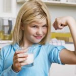 Young girl drinking milk showing off muscles.