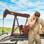 sad looking petroleum worker standing next to oil drill