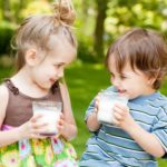 A young girl and boy drinking milk in a garden setting