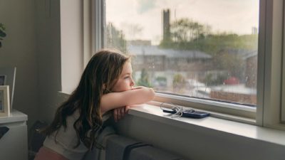 Young girl bored staring out the window at the rain in lockdown.