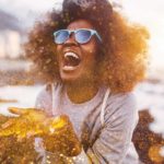 A woman blowing gold glitter out of her hands with a joyous smile on her face.