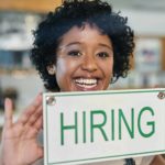 woman holding 'hiring' sign in shop