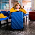 A sad woman sits leaning on her suitcase in a deserted airport lounge as the Qantas share price falls