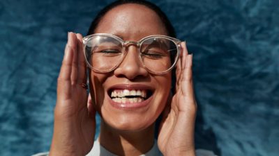 A woman raises her face to the sun while holding her glasses on her face with her hands.