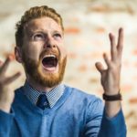 A smartly-dressed man screams to the sky in a trendy office.