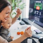 A woman sits at her home computer with baby on her lap, and the winning ticket in her hand.