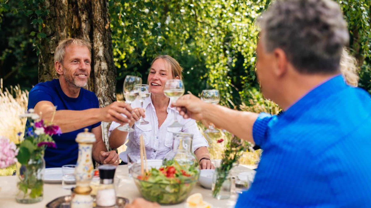 Group of people sitting around table outdoors and toasting glasses.