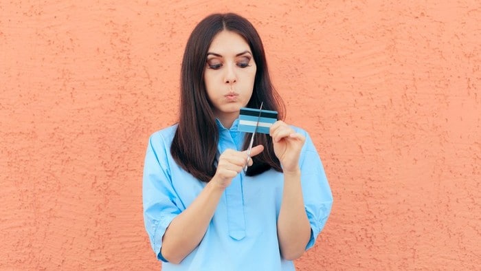 a woman with a narrow mouthed face looks down as she cuts her credit card with a pair of scissors.