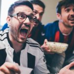 Man holding up betting slip and cheering along with two friends in front of TV