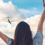 A woman looks up at a plane flying in the sky with arms outstretched as the Flight Centre share price surges