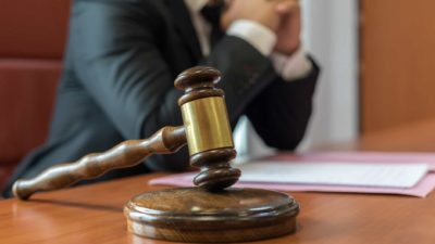 a gavel is placed on a stand on a desk with a legal representative wearing a suit in the background.