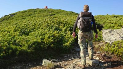 A mountaineer takes a rest while climbing a green mountain.