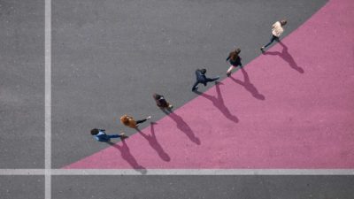 a view from above of six people walking along a curved upward line drawn on the ground between two axes.