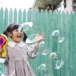 A little Asian girl is so excited by the bubbles coming out of her bubble machine.