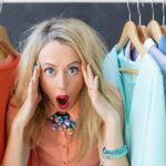 A woman peers through a bunch of recycled clothes on hangers and looks amazed.