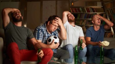 Four football fans put heads in hands and look disappointed while watching television.