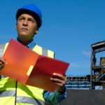 Australian Strategic Materials employee wearing a hard hat at a mine looks into the distance as he checks a folder.