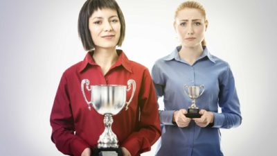 Winning woman smiles and holds big cup while losing woman looks unhappy with small cup