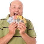 a man wearing casual clothes fans a selection of Australian banknotes over his chin with an excited, widemouthed expression on his face.