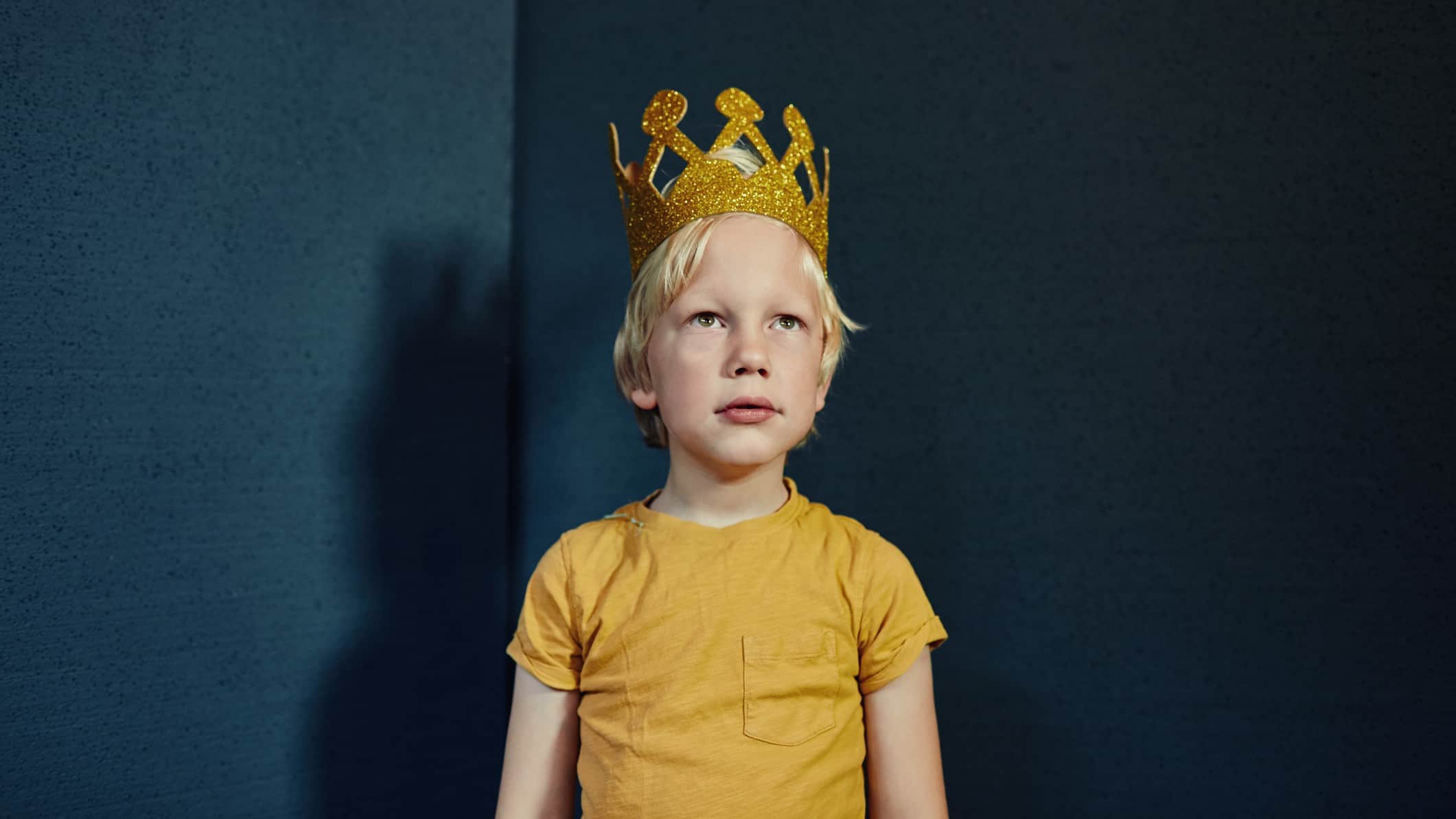 A boy with a gold crown stands stoically looking straight ahead.