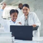 Two scientists in a Rhythm Biosciences lab cheer while looking at results on a computer.