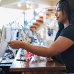 A young woman in a shop hands her credit card to the cashier